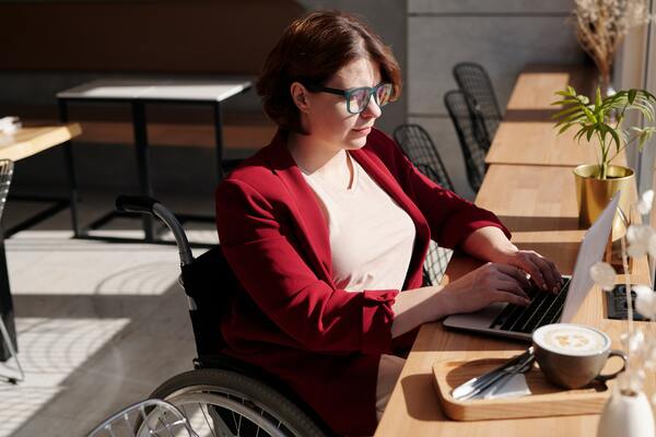 A imagem contém uma trabalhadora usuária de cadeira de rodas exercendo um dos tipos de trabalho em seu computador.