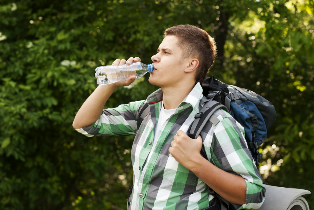 Rapaz bebendo água e com uma mochila nas costas. 